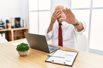 Wall Mural - Senior man working at the office using computer laptop covering eyes with hands and doing stop gesture with sad and fear expression. embarrassed and negative concept.