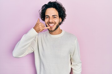 Handsome hispanic man wearing casual white sweater smiling doing phone gesture with hand and fingers like talking on the telephone. communicating concepts.