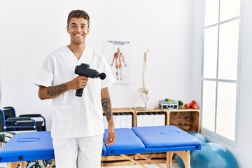 Sticker - Young hispanic man working as physiotherapist holding massage gun at physiotherapy room