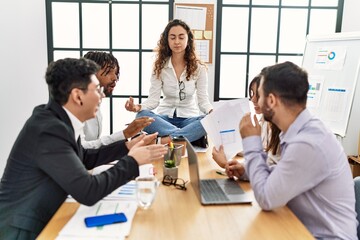 Wall Mural - Businesswoman enjoys meditating during meeting. Sitting on desk near arguing partners at the office.