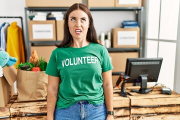 Sticker - Young brunette woman wearing volunteer t shirt at donations stand angry and mad screaming frustrated and furious, shouting with anger. rage and aggressive concept.