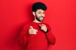 © Krakenimages.com - Young arab man with beard wearing casual red sweater pointing fingers to camera with happy and funny face. good energy and vibes.