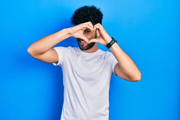 Canvas Print - Young arab man with beard wearing casual white t shirt doing heart shape with hand and fingers smiling looking through sign