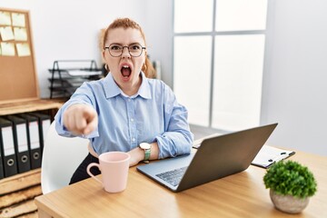 Canvas Print - Young redhead woman working at the office using computer laptop pointing displeased and frustrated to the camera, angry and furious with you