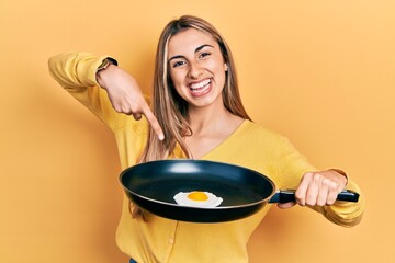 Poster - Beautiful hispanic woman cooking fried egg smiling happy pointing with hand and finger