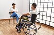 Two hispanic men physiotherapist and patient sitting on wheelchair having rehab session at clinic
