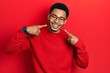 © Krakenimages.com - Young african american man wearing casual clothes and glasses smiling cheerful showing and pointing with fingers teeth and mouth. dental health concept.