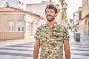 Poster - Young hispanic man standing at the street looking away to side with smile on face, natural expression. laughing confident.