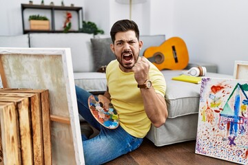 Poster - Young man with beard painting canvas at home angry and mad raising fist frustrated and furious while shouting with anger. rage and aggressive concept.