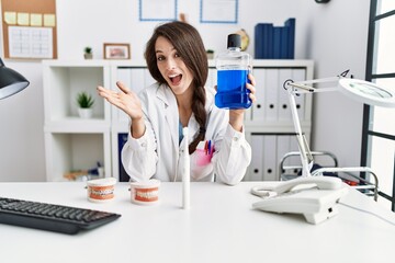 Poster - Young dentist woman holding mouthwash for fresh breath celebrating achievement with happy smile and winner expression with raised hand