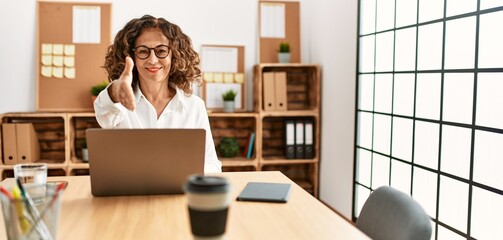 Canvas Print - Middle age hispanic woman working at the office wearing glasses smiling friendly offering handshake as greeting and welcoming. successful business.