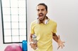 © Krakenimages.com - Young hispanic man wearing sportswear and drinking water at the gym angry and mad screaming frustrated and furious, shouting with anger. rage and aggressive concept.