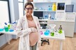 © Krakenimages.com - Young pregnant woman working at scientist laboratory looking positive and happy standing and smiling with a confident smile showing teeth