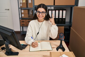 Poster - Young hispanic woman working at small business ecommerce wearing headset smiling with an idea or question pointing finger with happy face, number one