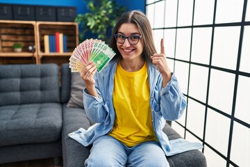 Poster - Young hispanic woman holding norwegian banknotes surprised with an idea or question pointing finger with happy face, number one