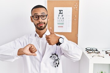 Poster - African american optician man standing by eyesight test doing thumbs up and down, disagreement and agreement expression. crazy conflict