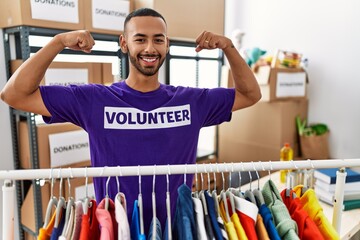 Poster - African american man wearing volunteer t shirt at donations stand showing arms muscles smiling proud. fitness concept.