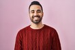 Young hispanic man with beard wearing casual sweater over pink background with a happy and cool smile on face. lucky person.