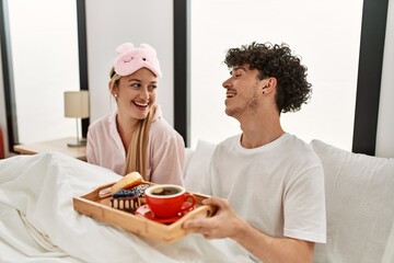 Poster - Young beautiful couple smiling happy having breakfast on the bed at home.