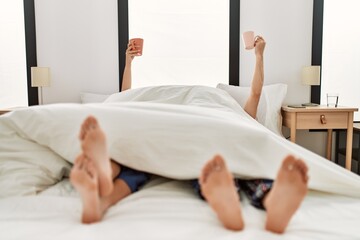 Poster - Couple awake under blanket. Having breakfast holding cup of coffee raised up on the bed.