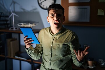 Wall Mural - Non binary person using touchpad device at night angry and mad screaming frustrated and furious, shouting with anger. rage and aggressive concept.