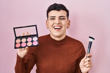 Canvas Print - Non binary person holding makeup brush and blush smiling and laughing hard out loud because funny crazy joke.