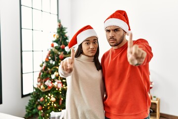 Sticker - Young hispanic couple standing by christmas tree pointing with finger up and angry expression, showing no gesture