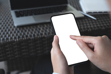 Wall Mural - Cell phone blank white screen mockup. Woman hands holding, using mobile phone at coffee shop, template for advertisement