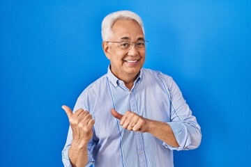 Wall Mural - Hispanic senior man wearing glasses pointing to the back behind with hand and thumbs up, smiling confident