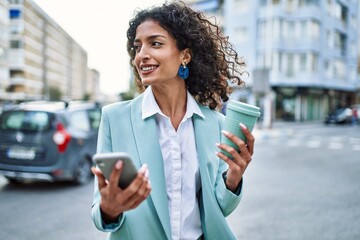 Wall Mural - Young hispanic business woman wearing professional look smiling confident at the city using smartphone