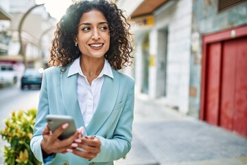 Wall Mural - Young hispanic business woman wearing professional look smiling confident at the city using smartphone