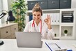 © Krakenimages.com - Young doctor woman wearing doctor uniform working using computer laptop doing ok sign with fingers, smiling friendly gesturing excellent symbol
