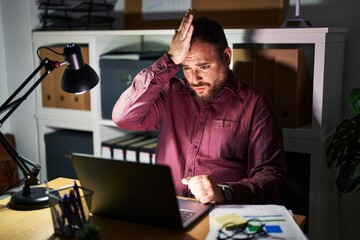 Canvas Print - Plus size hispanic man with beard working at the office at night surprised with hand on head for mistake, remember error. forgot, bad memory concept.