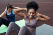 © etonastenka - Two young different women go in for sports outdoors in the stadium. ab crunches