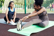 © etonastenka - Two lovely young women stretch while sitting on yoga mats before training outdoors. Girlfriends go in for sports at the stadium