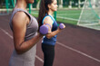 © etonastenka - Young diverse women pump arm muscles with dumbbells in the outdoor stadium. Close up