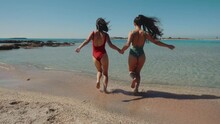 Pretty Female Friends Running Holding Hands By Sea On Sandy Tropical Beach In Swimsuits. Fitted Women In Bikini Walk Tanning On Summer Day Outdoors. Bikini Slow Motion. Lesbian LGBT Girls Admiring Sea