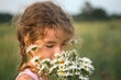 Portrait cute child girl with a bouquet of chamomile in summer on a green natural background. Happy child, hidden face, no face, covered with flowers. Copy space. Authenticity, rural life, eco-friendl