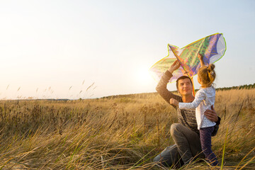 Dad helps his daughter to fly a kite in a field in the summer at sunset. Family entertainment outdoor, Father's Day, Children's Day. Rural areas, support, mutual assistance. Orange light of the sun