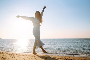 Wall Mural - Young woman walks along the seashore. The girl looks at the magical sunrise. Travel, weekend, relax and lifestyle concept.