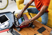 Close up hands of young african man packing luggage before going on vacation. Travel and vacation concept.