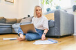 © baranq - Mid adult woman working from home sitting with laptop on the ground browsing documents