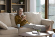 © fizkes - Middle-aged 50s woman relaxing alone in warm cozy living room holding smartphone read message, share sms, chatting in social media, web surfing helpful information on internet. Leisure, tech concept