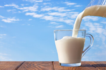 Wall Mural - milk pouring from jug into glass cup on table