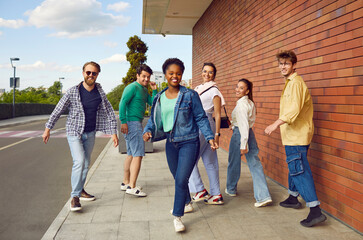 Whole squad back in town. Bunch of happy young diverse friends walking on the street together. Group of joyful beautiful African American, Asian and Caucasian people enjoying friendly summer hangout