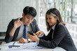 © crizzystudio - Two beautiful Asian businessmen working together in the office sitting at desk with a laptop working on paperwork to discuss the project's financial reports. business organization cooperation concept