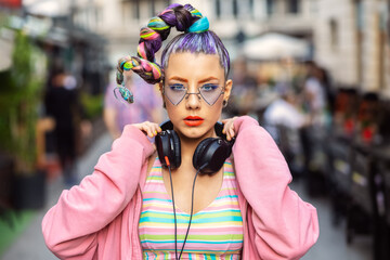 Cool funky young woman with trendy eyeglasses listening music on headphones outdoor