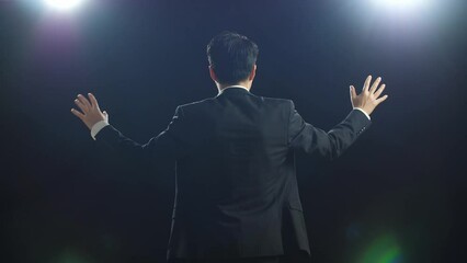 back view of asian speaker man in business suit showing index fingers up while speaking in the black