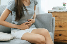 Asian Young Woman Suffering Stomach Ache Sitting On Couch In Living Room At Home, People Painful Stomachache, Gynecology, Menstrual Pain , Medical And Health Care Concept