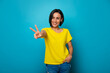 © My Ocean studio - Photo of happy beautiful young girl with stylish hairstyle in yellow t-shirt while she shows victory sign and isolated on blue background in studio